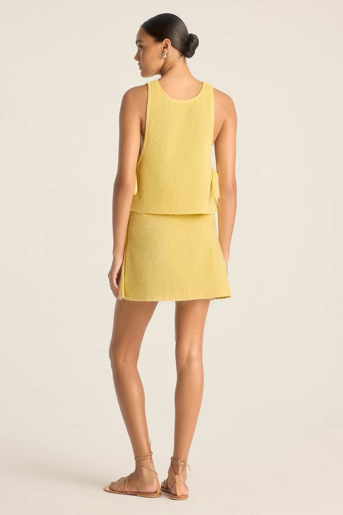 Woman faced away wearing a yellow terry cloth tank top with a matching wrap skirt 