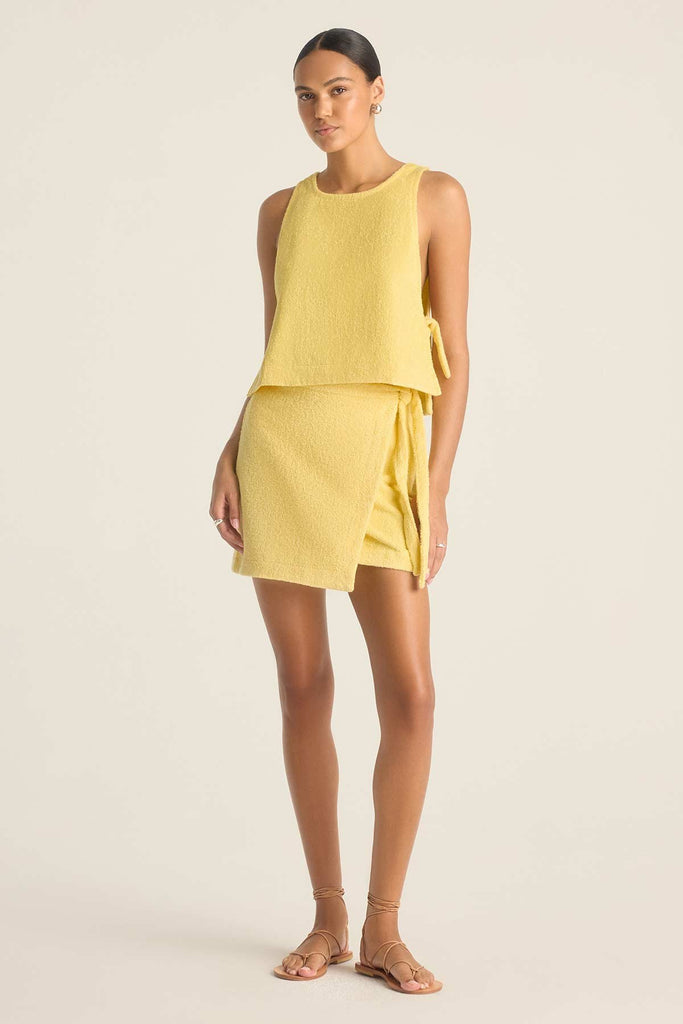 Woman wearing a yellow terry cloth tank top with a matching wrap skirt 