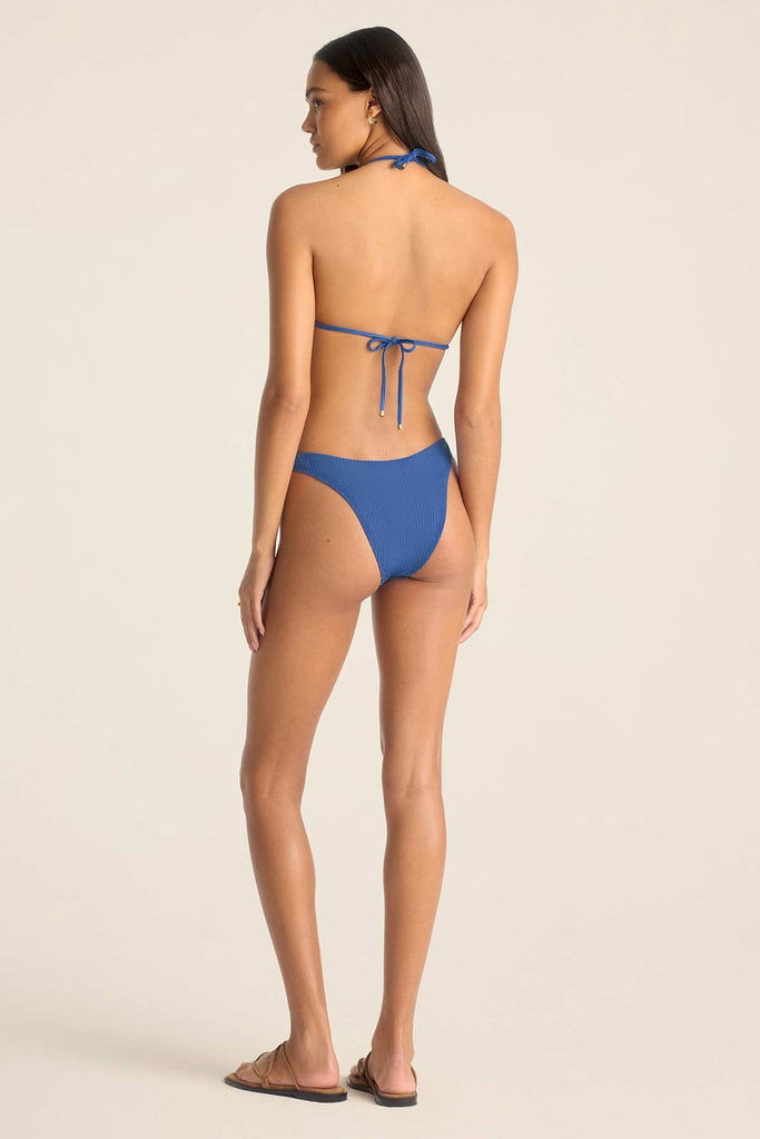 Woman turned away wearing a blue bikini top with O ring details with matching swim bottoms