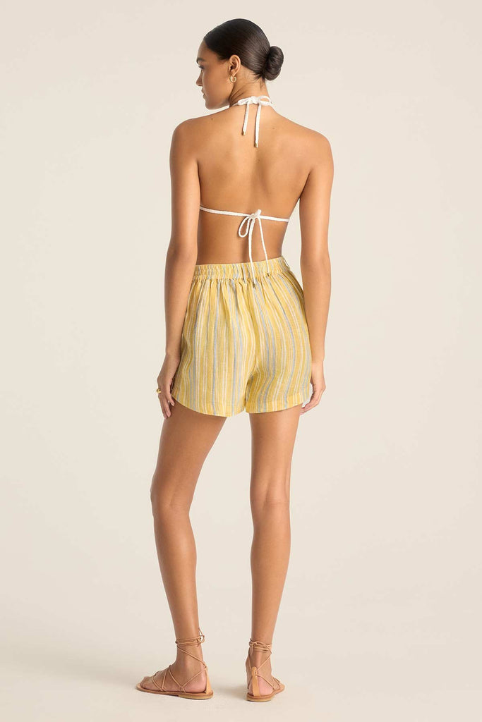 Woman faced away wearing a white string bikini top with yellow striped beach shorts