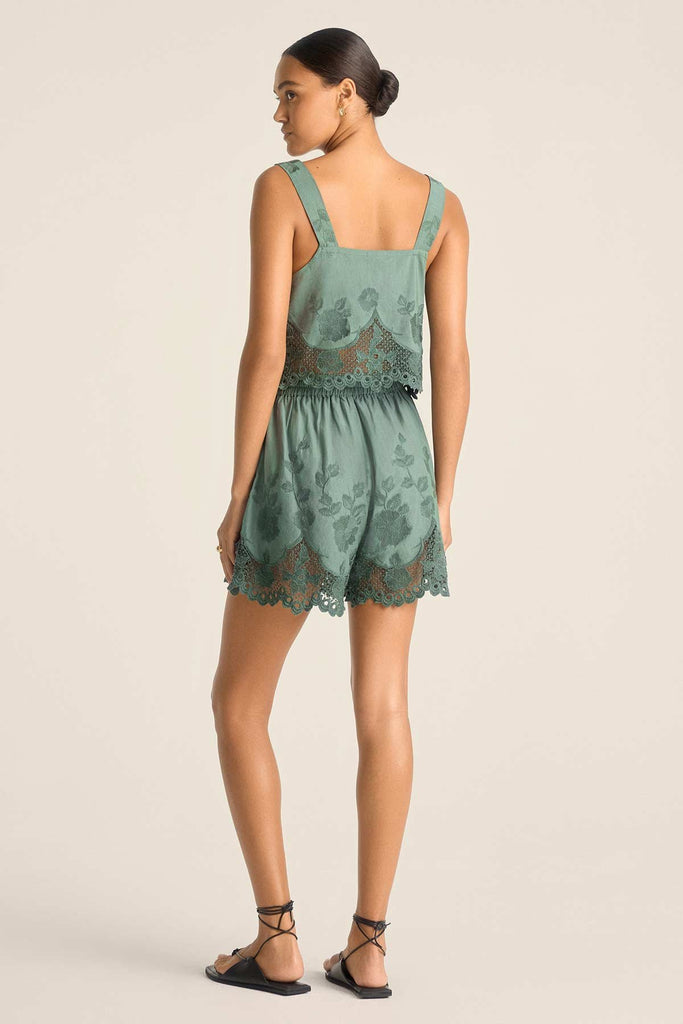 Woman turned away wearing a sea green lacy beach top with matching green beach shorts 