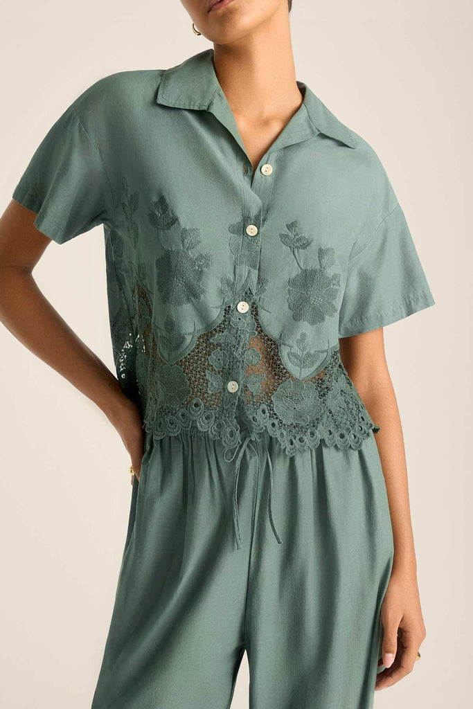 Woman wearing a sea green lacy short sleeve beach shirt with matching pants with a close up on the lace detail