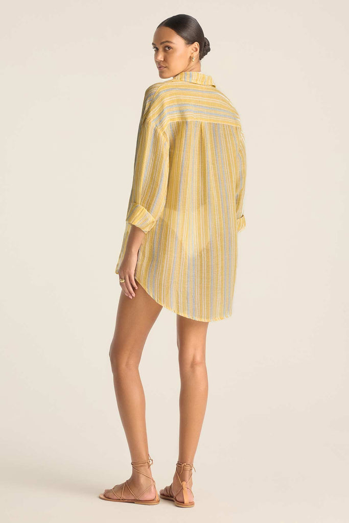 Woman turned away wearing a long sleeve button down beach shirt with yellow and blue stripes