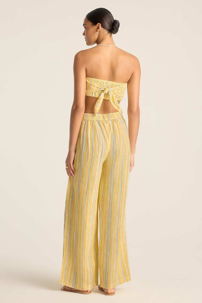 Woman faced away wearing a yellow and blue striped scarf beach top and matching beach pants