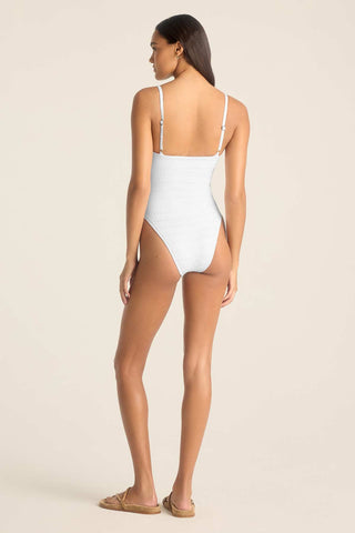 Woman turned away wearing a white one-piece swimsuit with adjustable straps