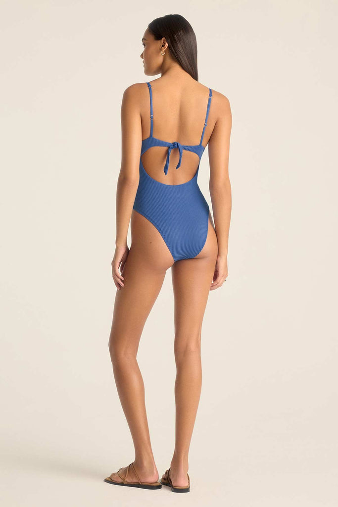 Woman turned away wearing a one-piece blue swimsuit with a tie back